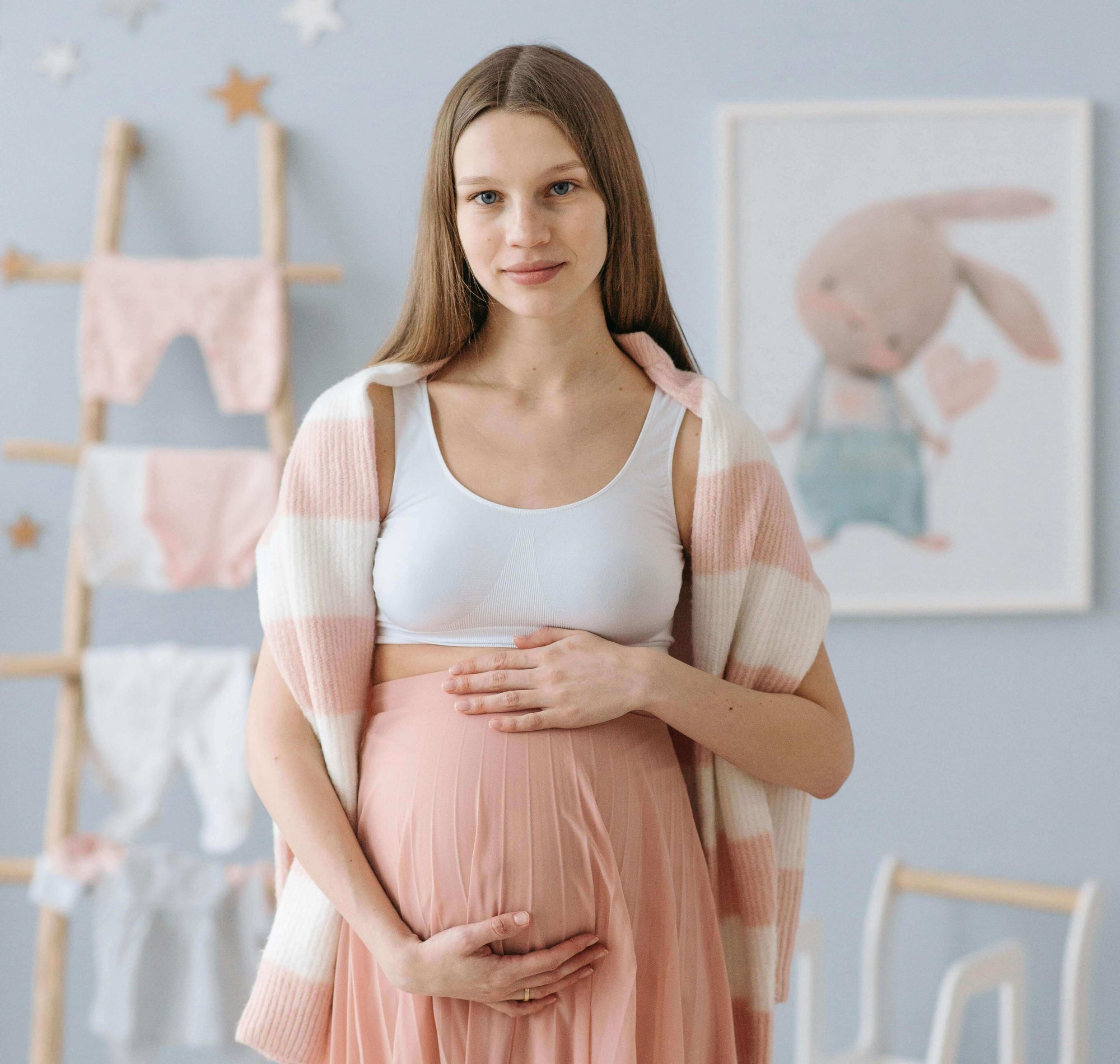 A pregnant woman stands confidently, showcasing important wearable electric breast pump features in a cozy nursery setting.